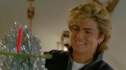 Sony Music George Michael hangs tinsel and other Christmas decorations in an outtake from the video for Last Christmas.