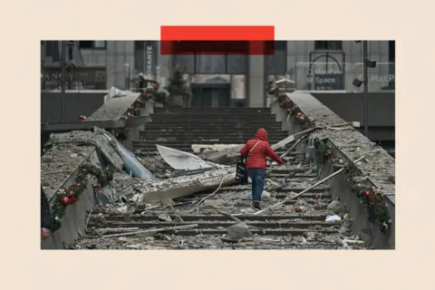 Getty Images A woman in a red coat climbs damaged steps after a Russian ballistic missile attack on Kyiv, Ukraine