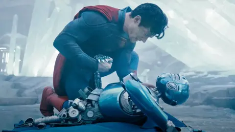 DC Studios/WB Superman holds the hand of a fallen humanoid robot in a still from the trailer