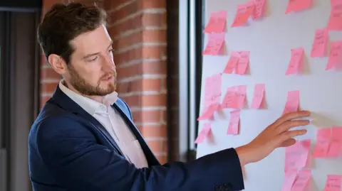 PA Consulting Charlie Paterson looks a white board covered in pink notes