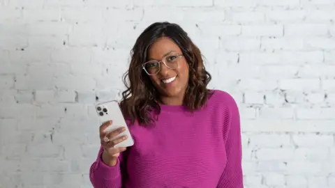 Megan Muir Andréa Jones smiling, holding up her phone and wearing a purple top.