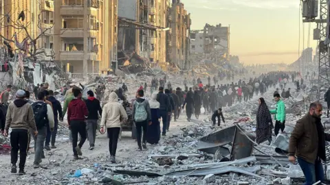 Getty Images Palestinians in Jabalia walk among debris as they return to their houses after the announcement of ceasefire and hostage-prisoner swap deal between Hamas and Israel