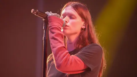 Getty Images Ethel Cain performing in a pink T shirt and jumper on stage