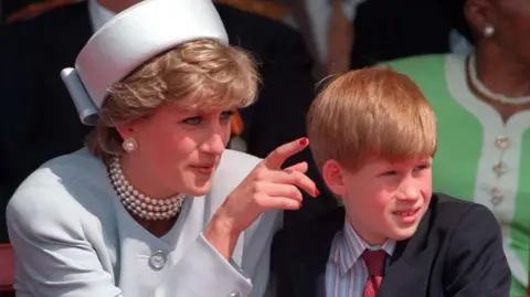 PA Media A young Prince Harry is pictured with his late mother, Diana, Princess of Wales, in 1995.  She is dressed in a pale jacket and matching hat. She has short hair and is wearing pearl earrings and a necklace. She is pointing to show something to Harry who is looking into the distance. He is wearing a dark suit jacket, a striped shirt and a red tie.