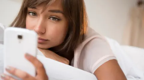 Getty Images A woman lying on her bed, checking her phone