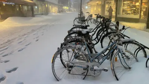 Maddy Savage Bicycles covered in snow stand in an almost deserted shopping street in Skellefteå.