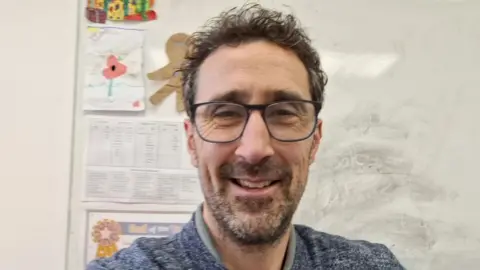 Steve Hitchcock Selfie photo of headteacher Steve Hitchcock. He is wearing glasses and has black hair and a beard and is smiling