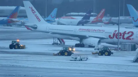 Reuters Staff use tractors to help clear snow from around aircraft after overnight snowfall caused the temporary closure of Manchester Airport