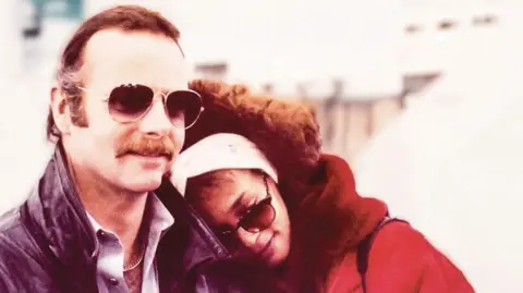 David Roberts / Courtesy of Chicago Review Press David Roberts with Whitney Houston. David has brown hair and a moustache and is wearing aviator sunglasses. Whitney has her head on David's shoulder. She is wearing dark glasses, a wide white head band and a red coat with a read fur collar.