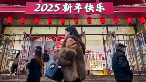 Getty Images Pedestrians walk past a shopping mall decorated with red lanterns and a sign reading 2025 Happy New Year to celebrate the upcoming Chinese New Year on January 14, 2025 in Chongqing, China.