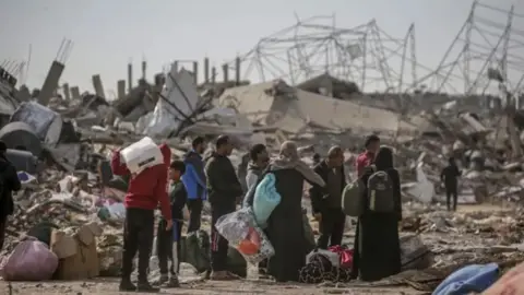 EPA Group of Palestinians carrying luggage and surrounded by rubble as they return to Rafah