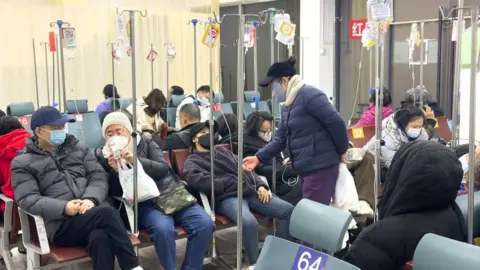 Getty Images Several masked patients wearing winter clothes sit at chairs to receive infusion therapy at a hospital in Shanghai on 27 December 2024. 