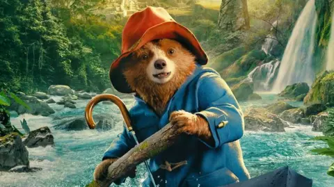 StudioCanal Paddington in Peru poster. Paddington bear is on a boat, on a river, which is running through a rainforest.