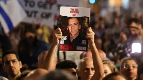 AFP File photo showing a man hold up a poster calling for the release of the body of Israeli soldier Oron Shaul, which was being held by Hamas in Gaza, at a rally in Tel Aviv, Israel (4 November 2023)