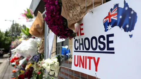 AFP Bouquets of flowers lie in the gaps of a metal gate, which has a sign reading 