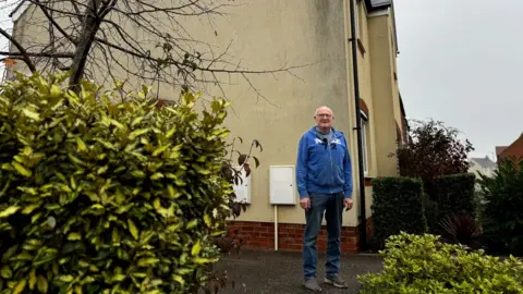 Robert Degavino stood in front of his Bellway home with a black stain on the wall behind him 