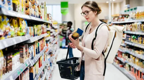 Getty Images A woman looks at a packet of biscuits in a supermarket - stock shot