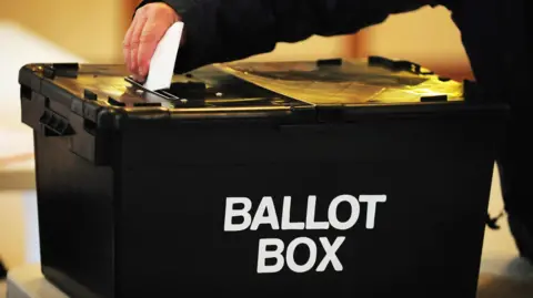 PA Media The hand of a voter wearing black places a ballot paper in the ballot box at a polling station.