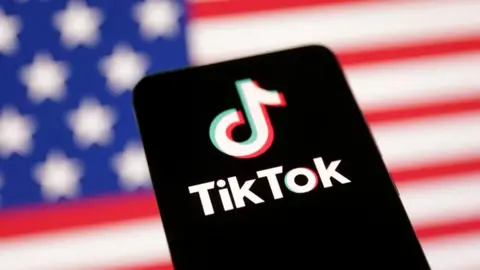 Reuters A phone displaying the logo of the popular social media platform TikTok is set in front of the American flag