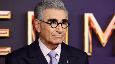 Getty Images  Eugene Levy attends the Emmy Awards wearing a purple tie, pink shirt and dark suit