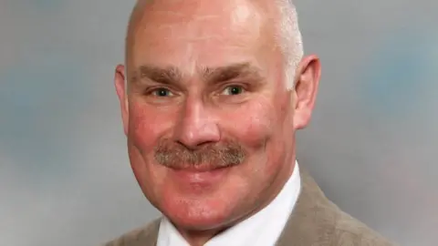 Derbyshire County Council Alex Stevenson smiles towards the camera in an official portrait as a councillor