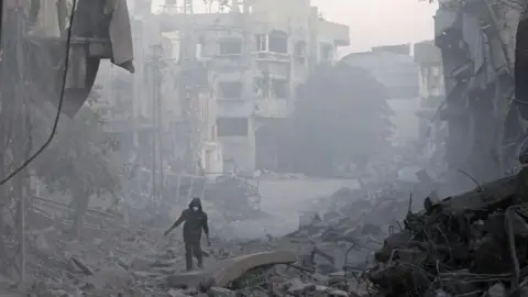 AFP A man walks through the rubble of buildings destroyed in Israeli air strikes at Bureij refugee camp, in central Gaza (12 January 2025)