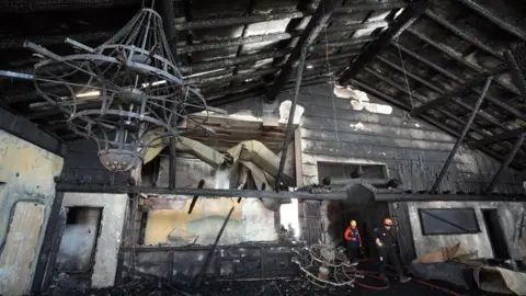 Evrim Aydin /Anadolu Two firefighters walk through a blackened, fire-damaged room in a hotel in the Bolu Kartalkaya Ski Resort in Turkey