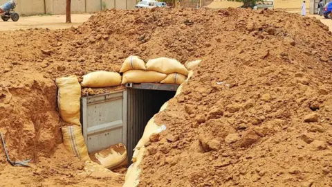 Mudathir Ibrahim Suleiman A bomb shelter in the compound of el-Fasher's Saudi Hospital - it shows corrugated iron sheets covered with orange soil and sand bags. 