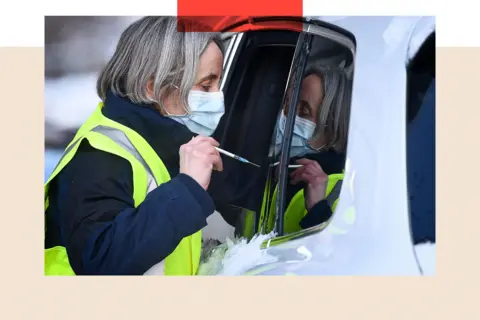 Getty Images A member of staff administers a COVID-19 vaccine to a member of the public through a car window of the public