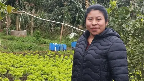 BBC Farmer Sandra Noemi Bucu Saz smiles at the camera as she stands in front of her plot of land