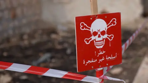 Red and white tape conrdoning off an area, close up of red sign with white skull. Sign reads: 