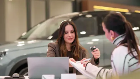 Getty Images Two women signing paperwork with a car in the background