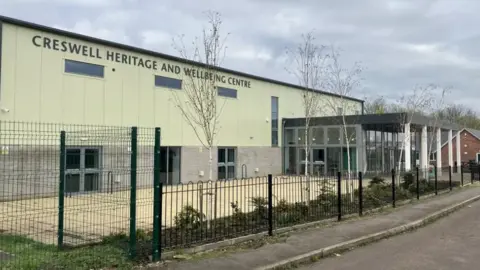 BBC A green-grey building behind fencing on the side of the road