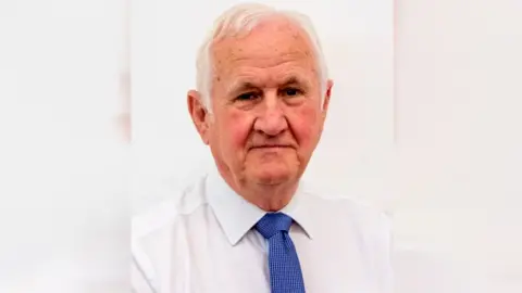 Bolsover District Council Councillor Duncan McGregor, a man with silver hair, wearing a white shirt and blue tie.