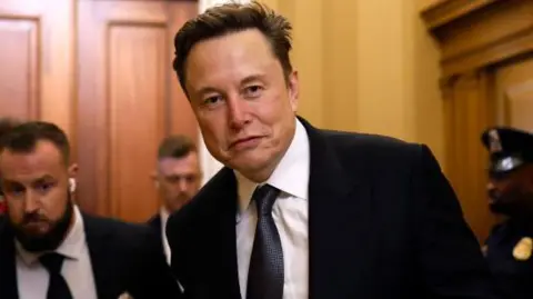 Getty Images Elon Musk, wearing a suit and holding a coffee, walks through the US Capitol building in Washington 