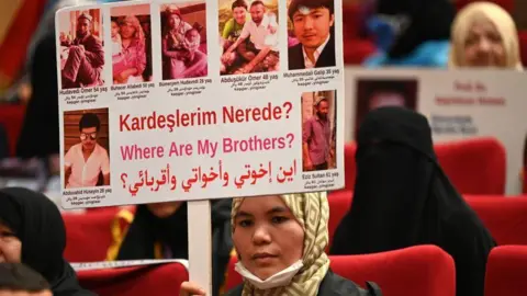 Getty Images A Muslim Uyghur woman holds up a sign with pictures of her brother and the word: Where are my brothers?