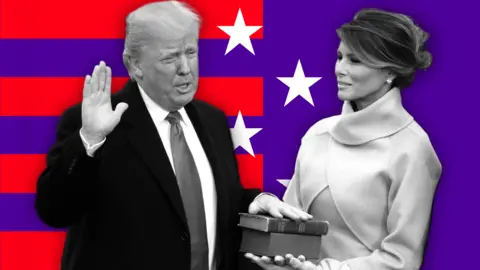 BBC Donald Trump, dressed in a suit and tie, places his hand on a Bible his wife Melania Trump is holding. They are standing before a background of red stripes and white stars on a purple background.