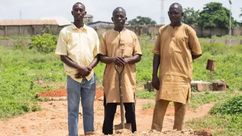 Ifiokabasi Ettang / BBC Magaji Abdullahi (C) with his hands rest on the handle of a spade standing in between his cousins and his two cousins Aliyu (L) and Abdullahi (R) at Tudun Wada graveyard in Kaduna state, Nigeria