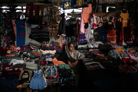 Getty Images A female stall owner at a Sri Lankan market looks into the distance, surrounded by the clothes she is selling