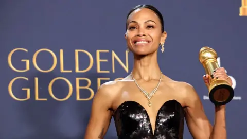 Reuters Zoe Saldaña holding up a Golden Globe trophy