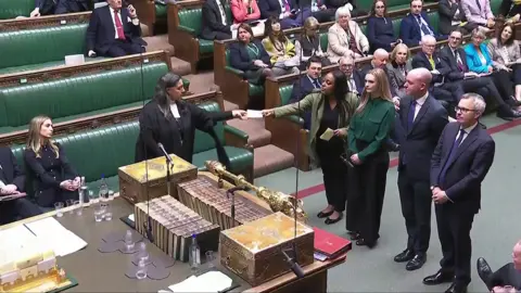 PA Media Four MPs line up side-by-side on the floor of the House of Commons to hand the result of a vote to a clerk. 