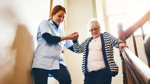 Getty Images Carer helps older woman down some stairs - they are both smiling