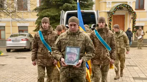 BBC/Xavier Vanpevenaege Soldiers hold a photo of Andriy Kusmenko outside the location of his funeral