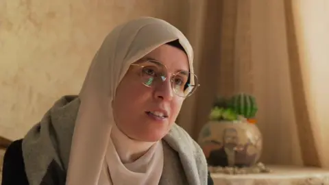 BBC Palestinian journalist Bushra al-Tawil wearing a cream headscarf and glasses at her family's apartment in Ramallah