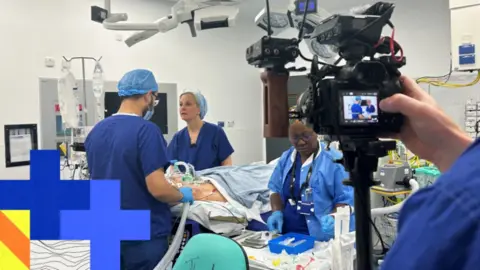 BBC News A BBC camera man is filming at an operating theatre at the Royal Free Hospital , filming complex cancer surgery taking place