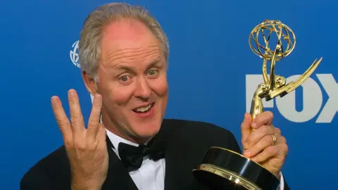 Getty Images John Lithgow holding up an Emmy trophy with one hand and holding up three fingers on his other hand at the Emmys in 1999