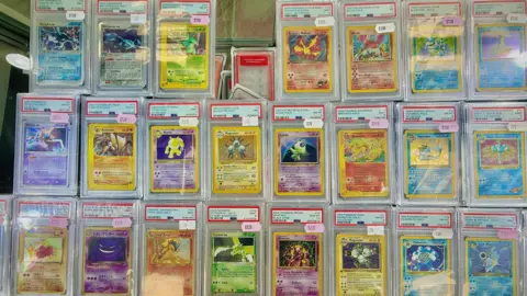 Danny Fullbrook/BBC Three rows of Pokemon cards. The top row has 7 cards, the other two have eight. It's a mix of different colours. All are sealed in plastic having been graded. They have values stuck on them, each is worth hundreds of pounds.