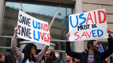 Getty Images People stand in front of the US Agency for International Development (USAID) with placards saying 