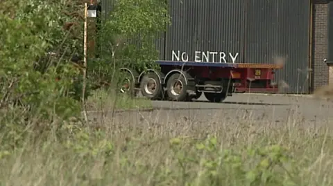 A truck trailers in a disused steelworks. Above the trailer is 