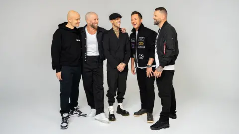 A picture of the boyband Five, posing together and laughing against a grey background